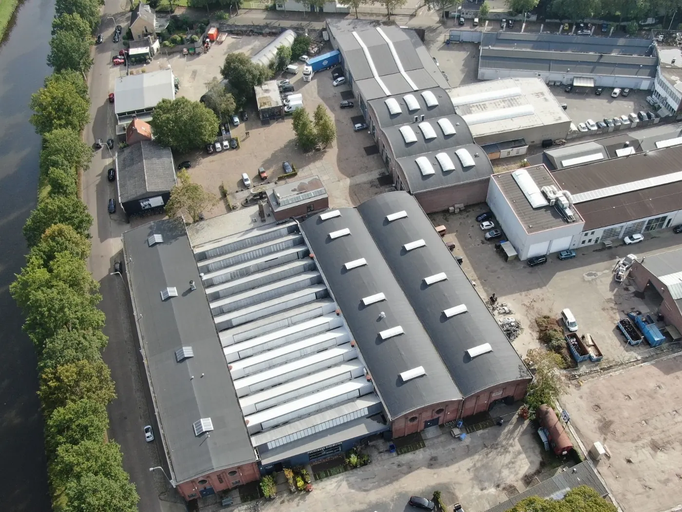 Luchtfoto van het terrein van FABRIEK59 aan het kanaal, met de lange hallen en de binnenplaats. Op elke unit waar een bedrijf zit staat een rode pin met het unitnummer; de bedrijven met een eigen pagina staan ook in de lijst ernaast.