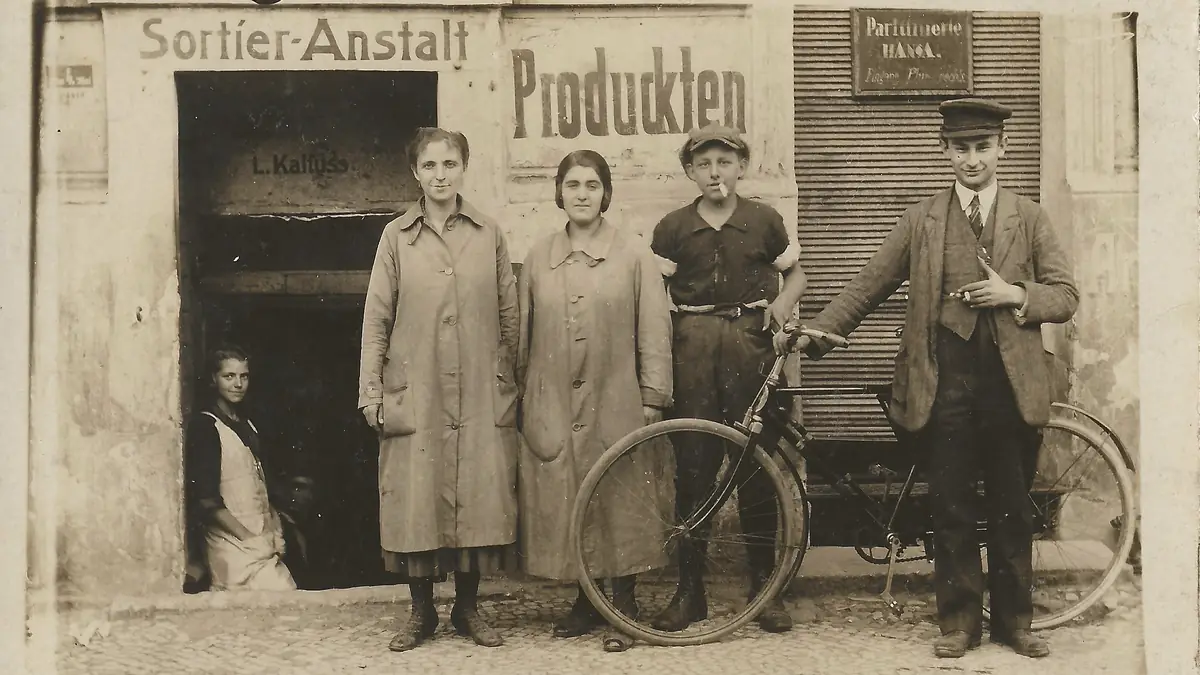 Gevel met de uithangborden Sortier-Anstalt en Produkten, vier personen en een fiets ervoor