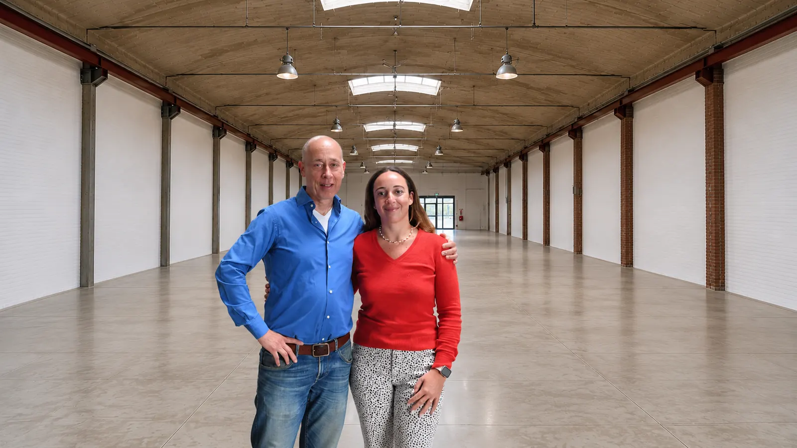 Greg Kalfus en zijn dochter Eline arm in arm in een lege hal met bakstenen kolommen en lichtstraten in het dak