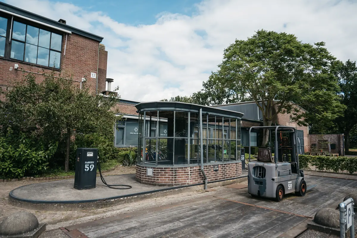 De glazen serre op de binnenplaats met de brandstofpomp ervoor, een heftruck ernaast en bakstenen bedrijfspanden op de achtergrond