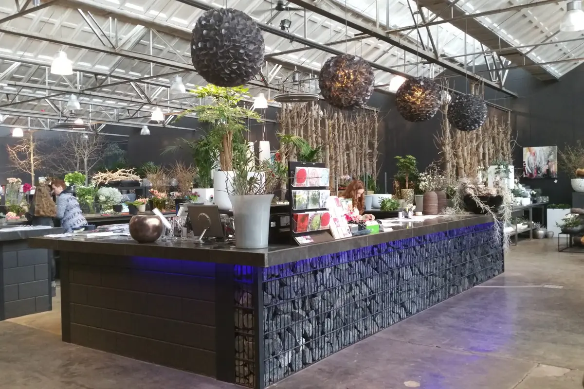 Showroom onder een spantendak met daklichten, met een lange balie van staalkorven gevuld met stenen en gevlochten bollampen erboven