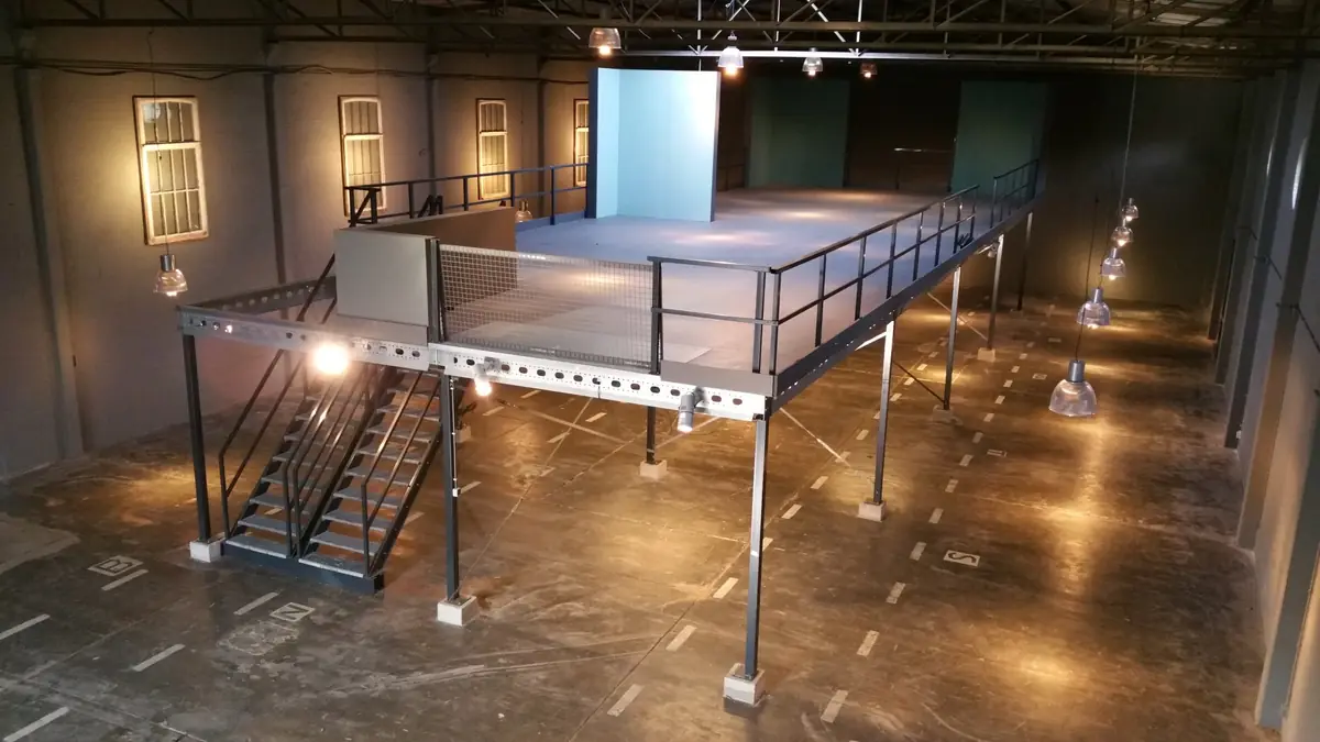 Lege fabriekshal met een stalen tussenvloer op poten, een trap ernaartoe en hanglampen aan de spanten