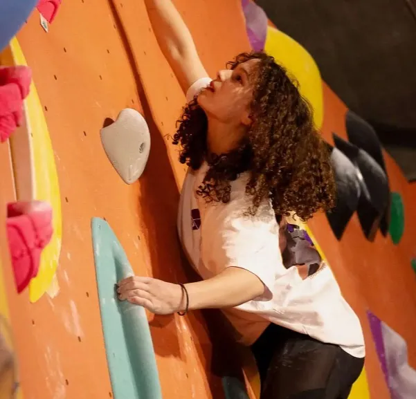Klimster met krullend haar aan een oranje boulderwand met gekleurde grepen