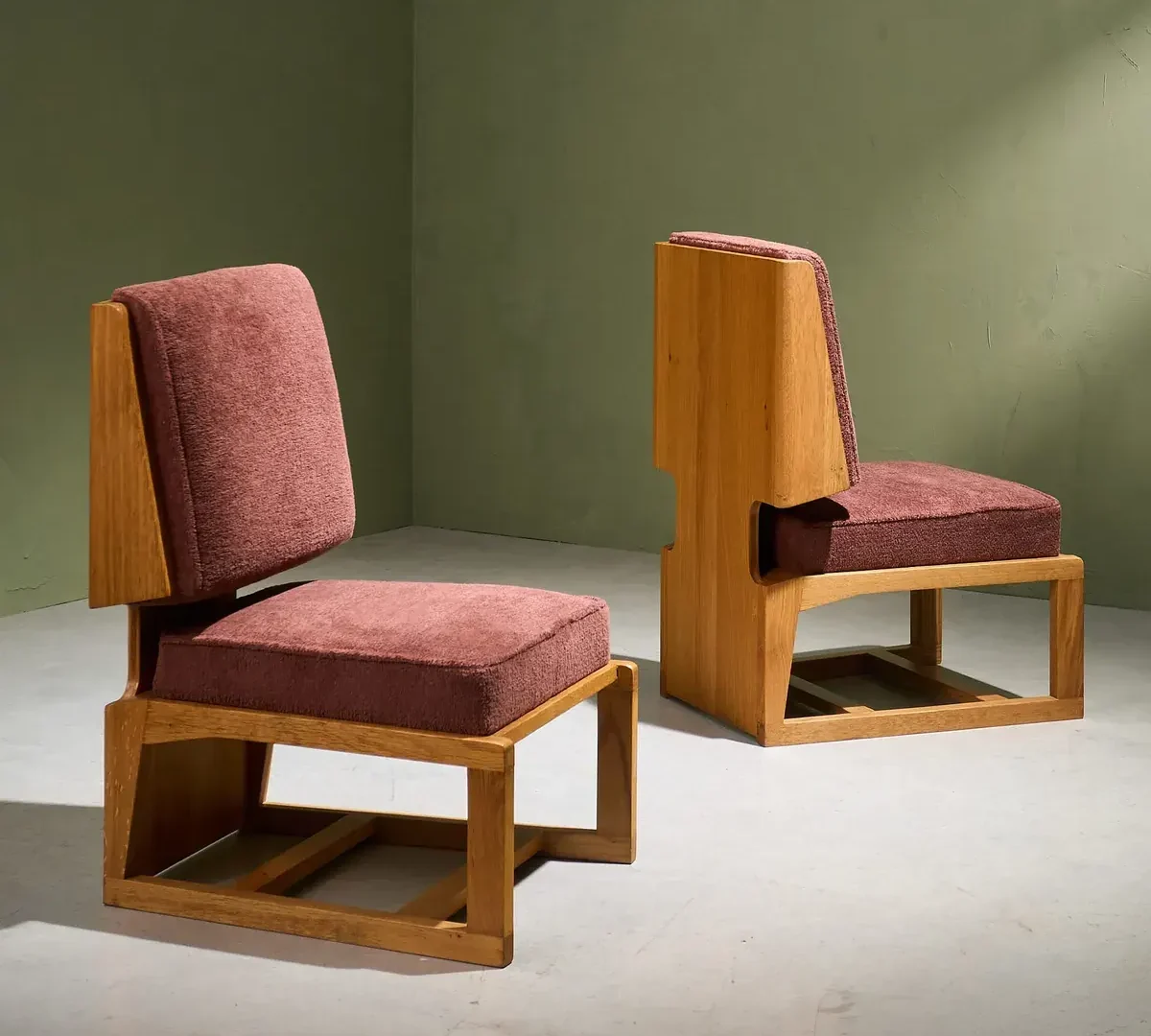 Twee fauteuils met een eikenhouten frame en oudroze bekleding tegen een groene wand