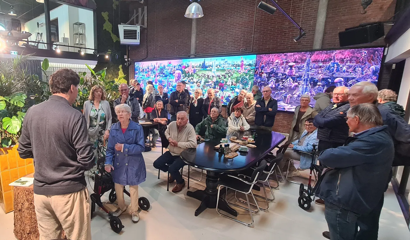 Een groep mensen rond een zwarte tafel voor een brede beeldschermwand met een kleurrijk tafereel